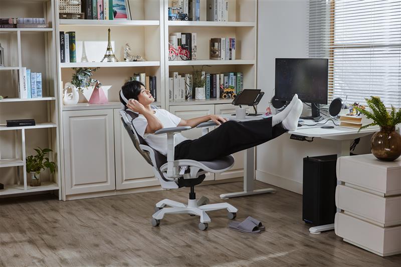 Picture showing a person sitting on a TGIF Ace Game white and relaxing with his feet on the desk and a headphones on his head